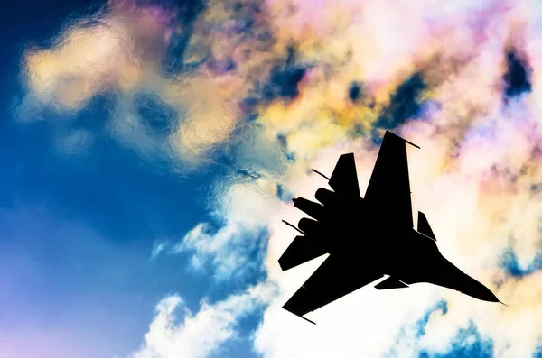 Silueta de un avión de combate sobre un fondo de nubes de cielo iridiscentes y sol — Foto de Stock