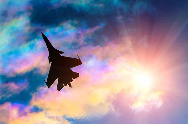 Silhouette of a fighter plane on a background of iridescent sky clouds and sun — Stock Photo, Image