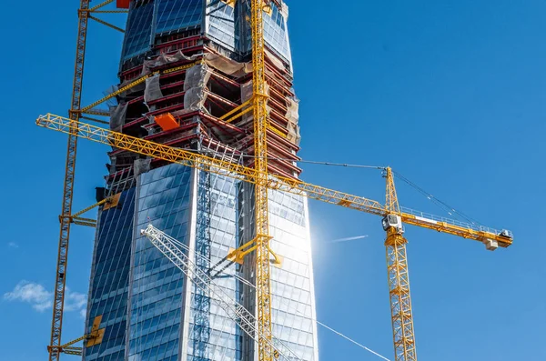 Schaal actieve skyscraper gebouw, schittering van de zon op de ramen, kranen tegen de blauwe hemel. — Stockfoto