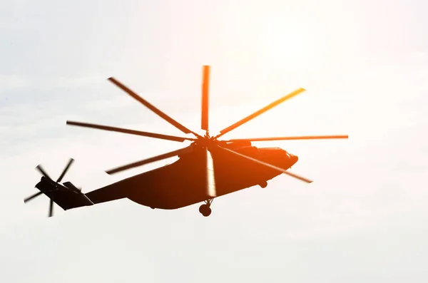 Huge silhouette of a helicopter flies up in the sky glare from the sun. — Stock Photo, Image