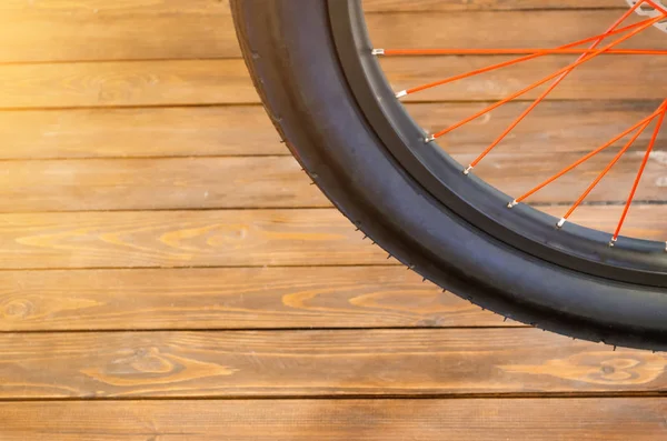 Das Rad eines stylischen Fahrrads mit schwarzer Felge und schwarzem Gummireifen, roten Speichen, stilvollem Holzhintergrund. — Stockfoto