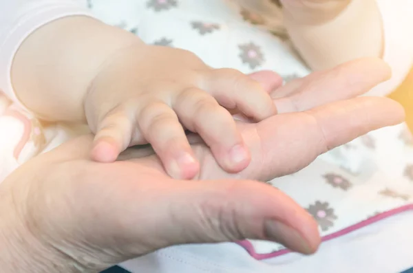 Barnets hand om en bebis å av en vuxen persons palm. Begreppet förhållandet mellan mormor och barnbarn — Stockfoto