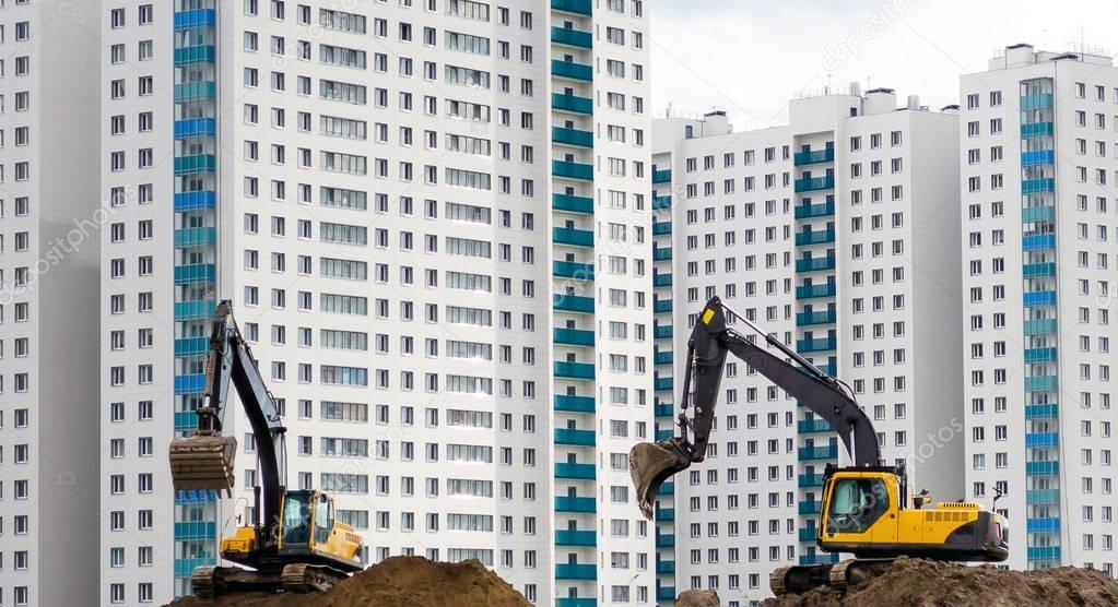 Excavators work on the sand on the background of multi-storey houses