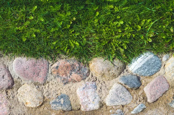 Antiguas adoquines en raras piedras en arena con hierba — Foto de Stock