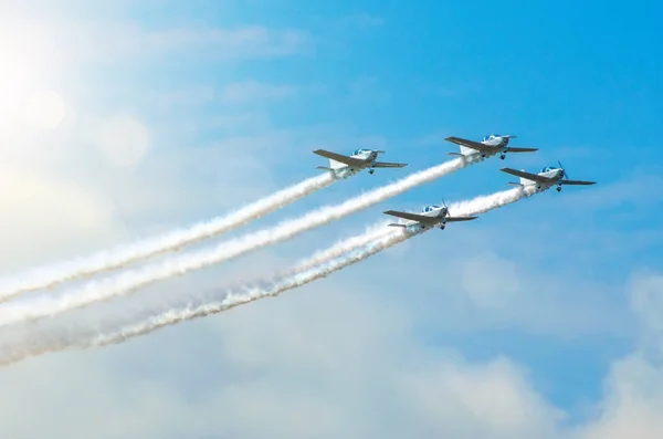 Avión de motor ligero con un rastro de humo blanco vuela en grupos en el cielo azul con luz solar y deslumbramiento —  Fotos de Stock