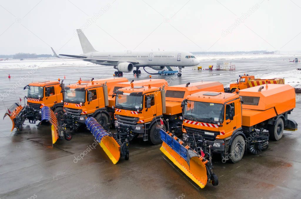 Snow-removal machine parked in a row in the background of a passenger airplane at the airport