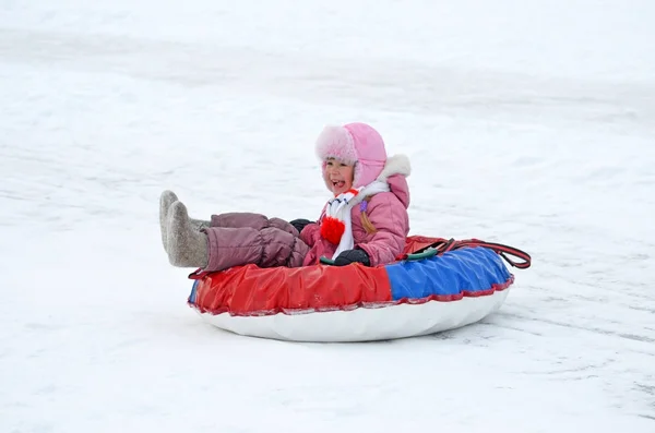 Klein meisje in laarzen en wanten rolt op de achtbaan in de winter. — Stockfoto