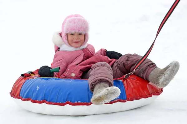 Klein meisje in laarzen en wanten rolt op de achtbaan in de winter. — Stockfoto