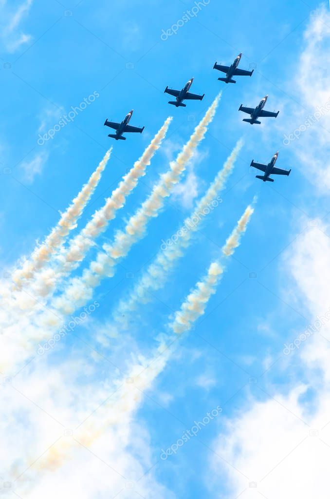 Group of fighter planes fly up with a smoke track against a blue sky with clouds.