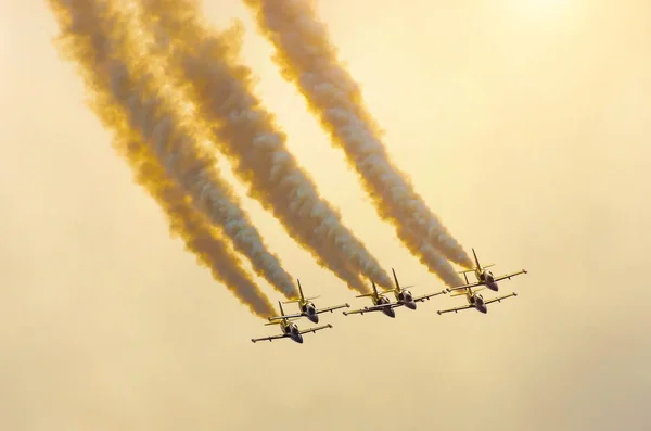 Ομάδα μαχητικά αεροπλάνα πετούν μέχρι με έναν καπνό κομμάτι πορτοκαλί ουρανό με σύννεφα. — Φωτογραφία Αρχείου