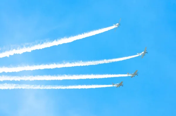 Avión de motor ligero con un rastro de humo blanco vuela en grupos en el cielo azul con luz solar y deslumbramiento . — Foto de Stock