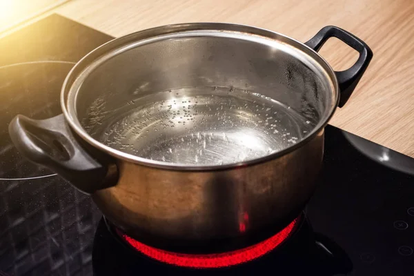 Metallpfanne mit kochendem Wasser auf dem Induktionsherd rote Herdplatte. — Stockfoto