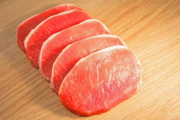 Cinco trozos de carne de cerdo picada en una tabla con una textura de madera . — Foto de Stock