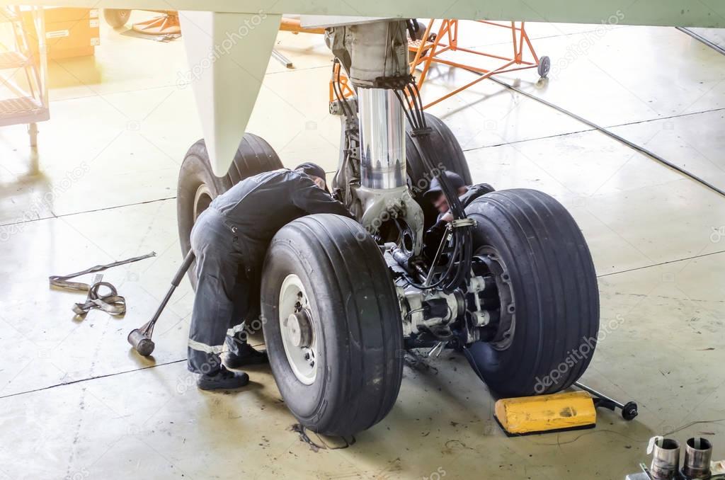 Repair of the chassis landing gear of the aircraft, two technicians of mechanics at work in the hangar.