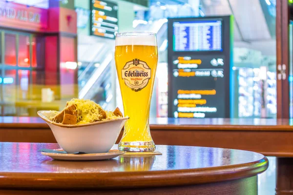 A glass of beer Edelweiss and a plate of breadcrumbs and cheese. In the background, online board displays flights to the airport. Russia. Moscow. January 13, 2018. — Stock Photo, Image