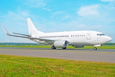 Beyaz yolcu uçak havaalanında, yeşil çim ön planda mavi bir gökyüzü çerçevede bir parça taksi sürmek.