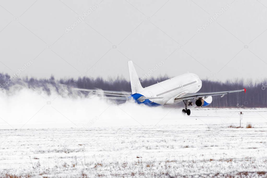 Airplane take off from the snow-covered runway airport in bad weather during a snow storm, a strong wind in the winter.