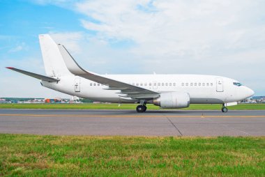 Beyaz yolcu uçak havaalanında, yeşil çim ön planda mavi bir gökyüzü çerçevede bir parça taksi sürmek.