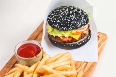 White paper ile patates kızartması ve bir ahşap tahta üzerinde domates soslu bir fincan siyah burger.