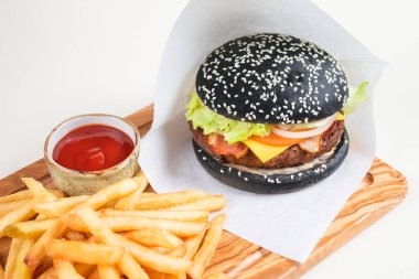 White paper ile patates kızartması ve bir ahşap tahta üzerinde domates soslu bir fincan siyah burger.