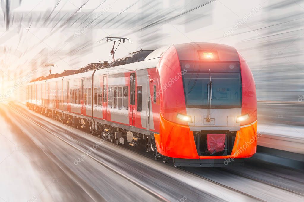 High speed train with luminous headlights and rides at high speed at the railway station in the city.