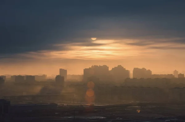 Silhouette of urban landscape with a disc of sun shining through low clouds of a polluted urban atmosphere. — Stock Photo, Image