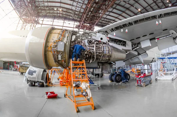 Specialist mechanic repairs the maintenance of a large engine of a passenger aircraft in a hangar. View of engine without bonnet, wing and landing gear. — Stock Photo, Image