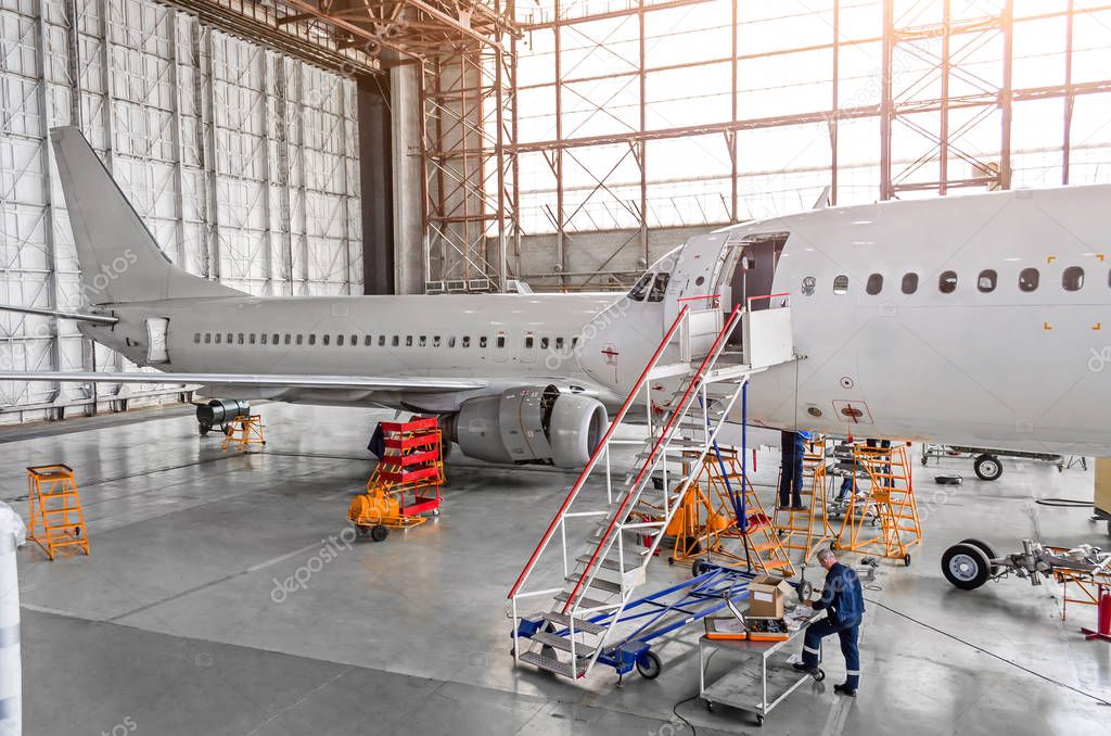 Aircraft during repair, technical inspection is a working technician. View of nose, a cockpit with a staircase leading into the entrance. In background, the other tail and fuselage of the airplane.