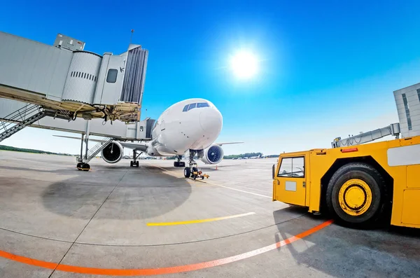 Parking at the airport, airplane at the teletrap. Aerodrome tractor is ready for towing and departure of the aircraft. Against the background of a blue sky and bright sun, nice weather. — Stock Photo, Image