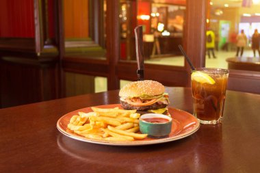 Patates kızartması ve bir bıçak ile burger orta-peynir bir grunge tabak içinde ketçap soslu piyano bir kadeh kokteyl dilim limon ve bir tübül ile sıkışmış.