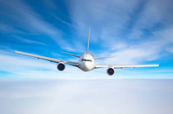 Passenger airplane flying at flight level high in the sky above the clouds and blue toned sky. View directly in front, exactly. Stock Picture