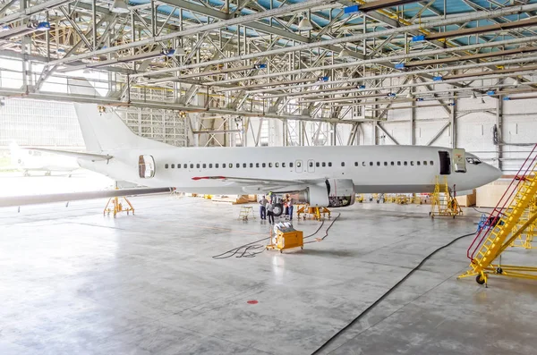 Passenger airplane on maintenance of engine, check repair in airport hangar. Aircraft side view, open hangar doors.