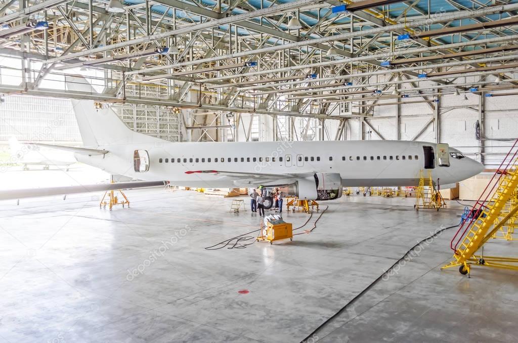 Passenger airplane on maintenance of engine, check repair in airport hangar. Aircraft side view, open hangar doors.
