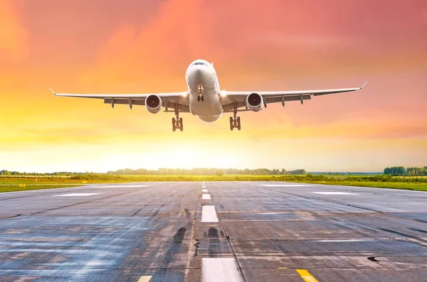 Grote lange afstand vliegtuigen deperture landing op een landingsbaan in de avond tijdens een heldere rode zonsondergang. — Stockfoto