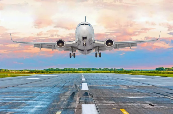 Avião voando chegada pousando em uma pista à noite durante um pôr do sol rosa brilhante . — Fotografia de Stock