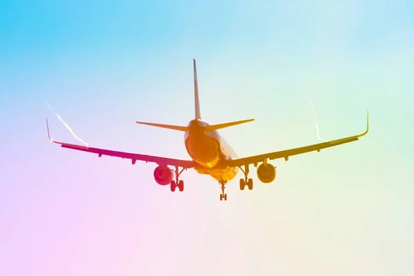 Avión de pasajeros vuela cerca del resplandor del sol con un gradiente de arco iris de color en el aterrizaje, con las alas de un vórtice de chorro de vapor . — Foto de Stock