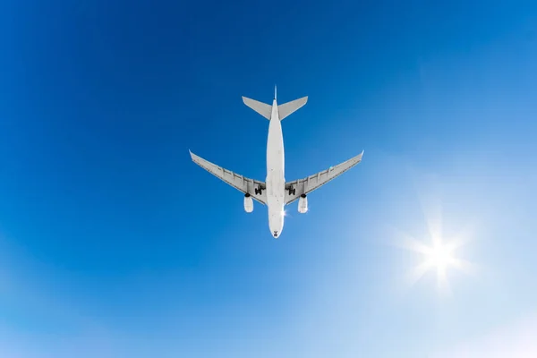 Gran avión blanco de pasajeros vuela en un cielo azul con un sol brillante . — Foto de Stock