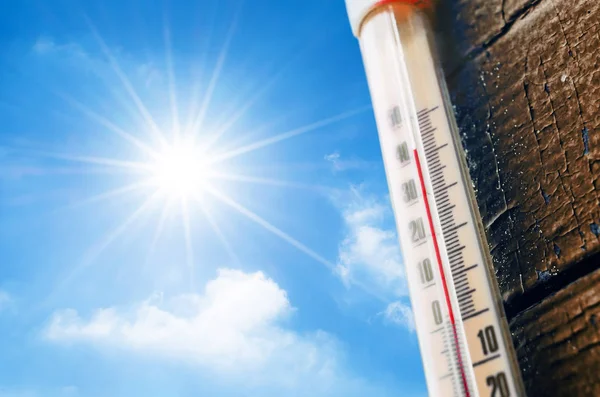 Thermomètre avec une lecture à haute température sur une échelle, sur un fond de soleil brillant et un ciel bleu avec des nuages. Le concept de temps chaud et dangereux, réchauffement climatique. — Photo