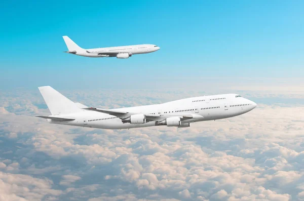 Δύο μεγάλα άσπρα επιβατηγά αεροπλάνα πετούν παράλληλα με το άλλο στον ουρανό πάνω από τα σύννεφα. — Φωτογραφία Αρχείου