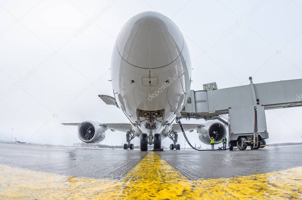 Commercial passenger airplane in the parking at the airport with a nose forward and a gangway - front view.