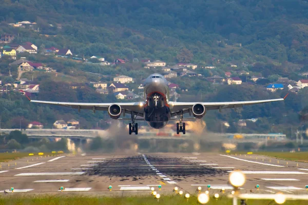 Vista da extremidade da pista do aeroporto, e um avião de descolagem contra o pano de fundo de montanhas e casas . — Fotografia de Stock