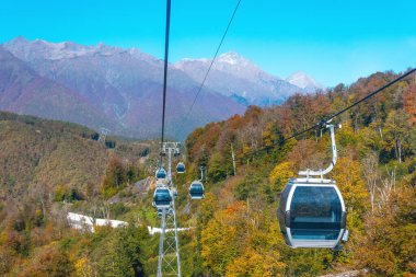 Kayak asansörleri ve turistler için kulübeleri olan Cableway, şehir manzarası ve dağlardaki sonbahar ormanı.