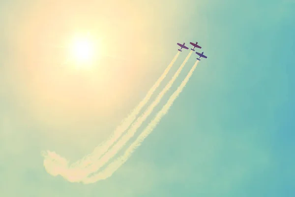 Groep van drie turbopropvliegtuigen vliegen in de lucht zon schijnen verlaten van een witte rokerige spoor. — Stockfoto