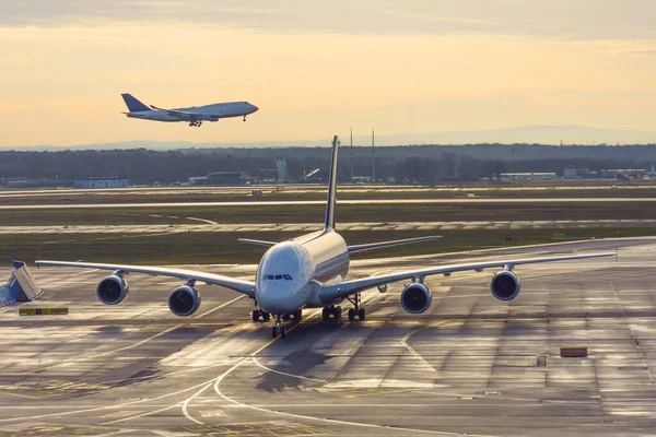 Frontansicht eines großen Flugzeugs auf Lenkschienen und Parkplätzen am Flughafen nach der Landung, im Hintergrund ein weiteres Flugzeug, das auf der Landebahn landet. — Stockfoto