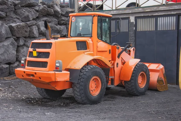 Un tractor naranja con un cubo delante está estacionado en las montañas . — Foto de Stock