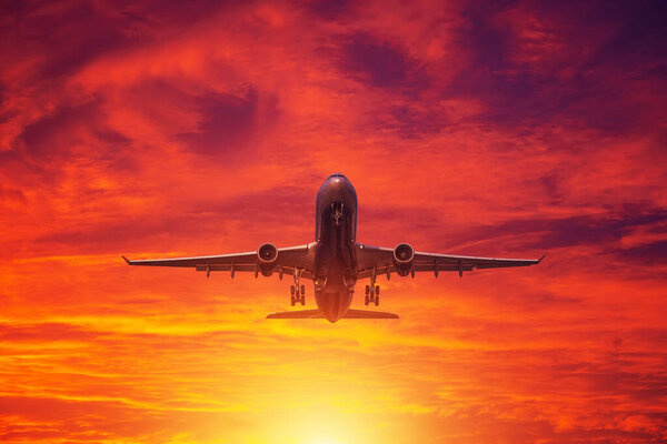 Airplane takes off from the airport on the background of evening clouds and btight red sunset