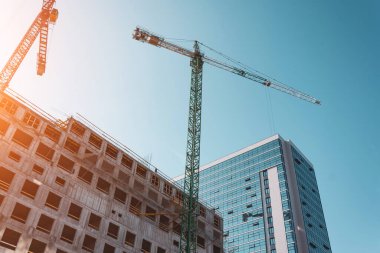 Yüksek inşaat vinçleri ve arka planında cam kulesi olan inşaat halindeki bir binanın görüntüsü.