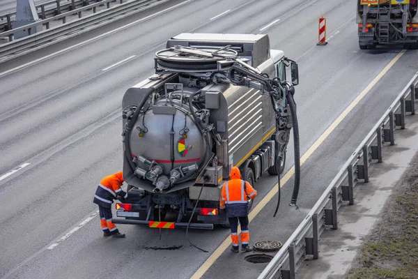Sludge washer truck and workers specialists at work on the side of the highway to clean underground infrastructure, eliminate blockages in the sewer road sewage into the collector — Stock Image Sludge Washer Truck Workers Specialists Work Side Highway Clean Underground Stock Photo