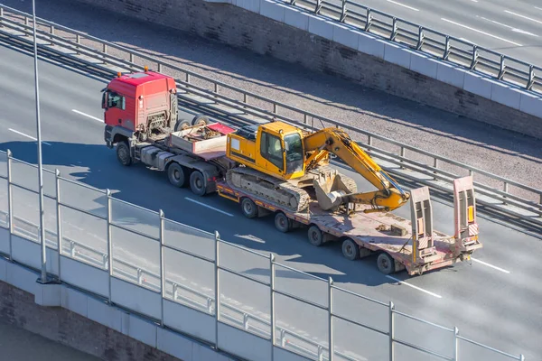 Excavator on transportation trailer truck with long trailer platform on the bridge highway in the city