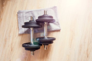 İki dambıl yere uzanıyor, bir havluyla, evde egzersiz yapıyor.